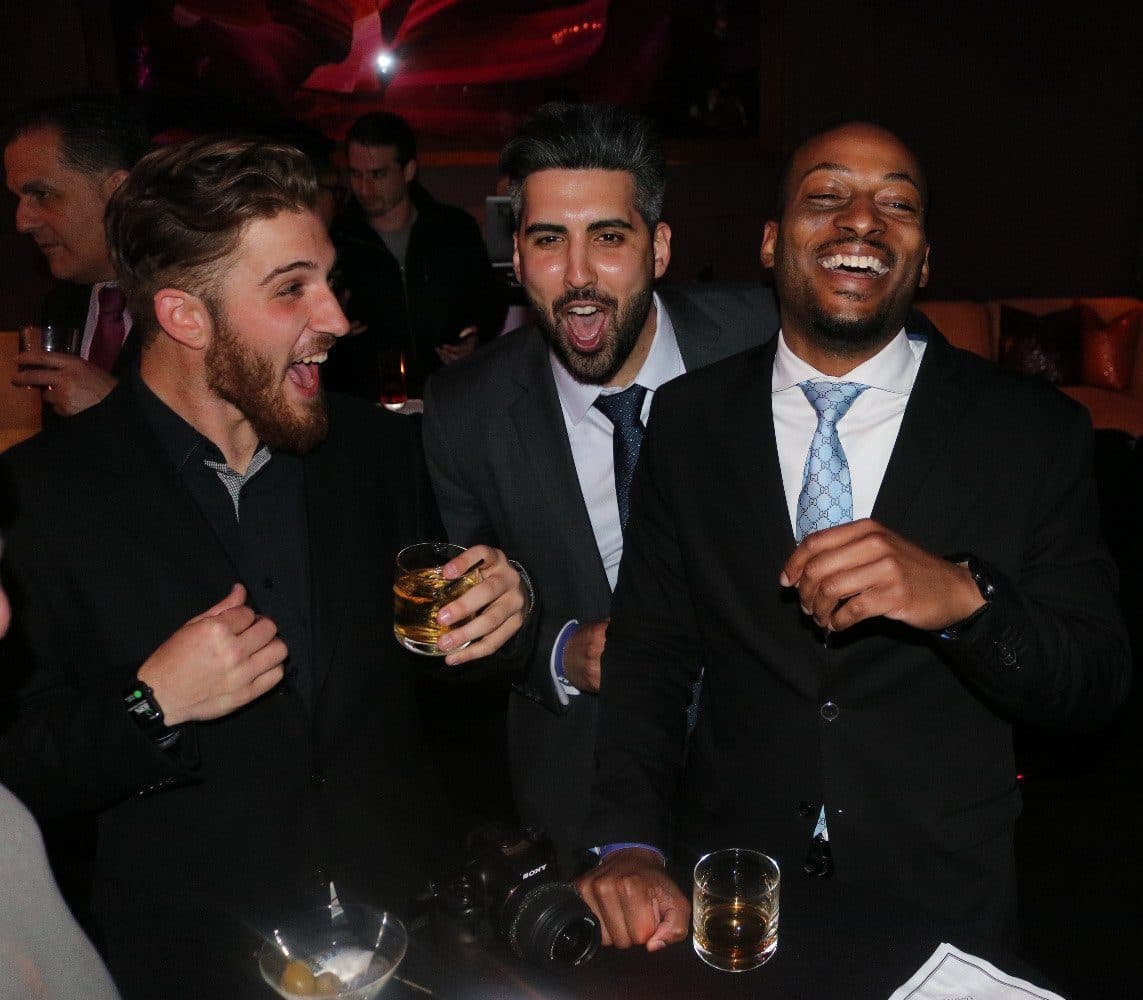 Group of men in formal suits laughing and having drinks at a party.
