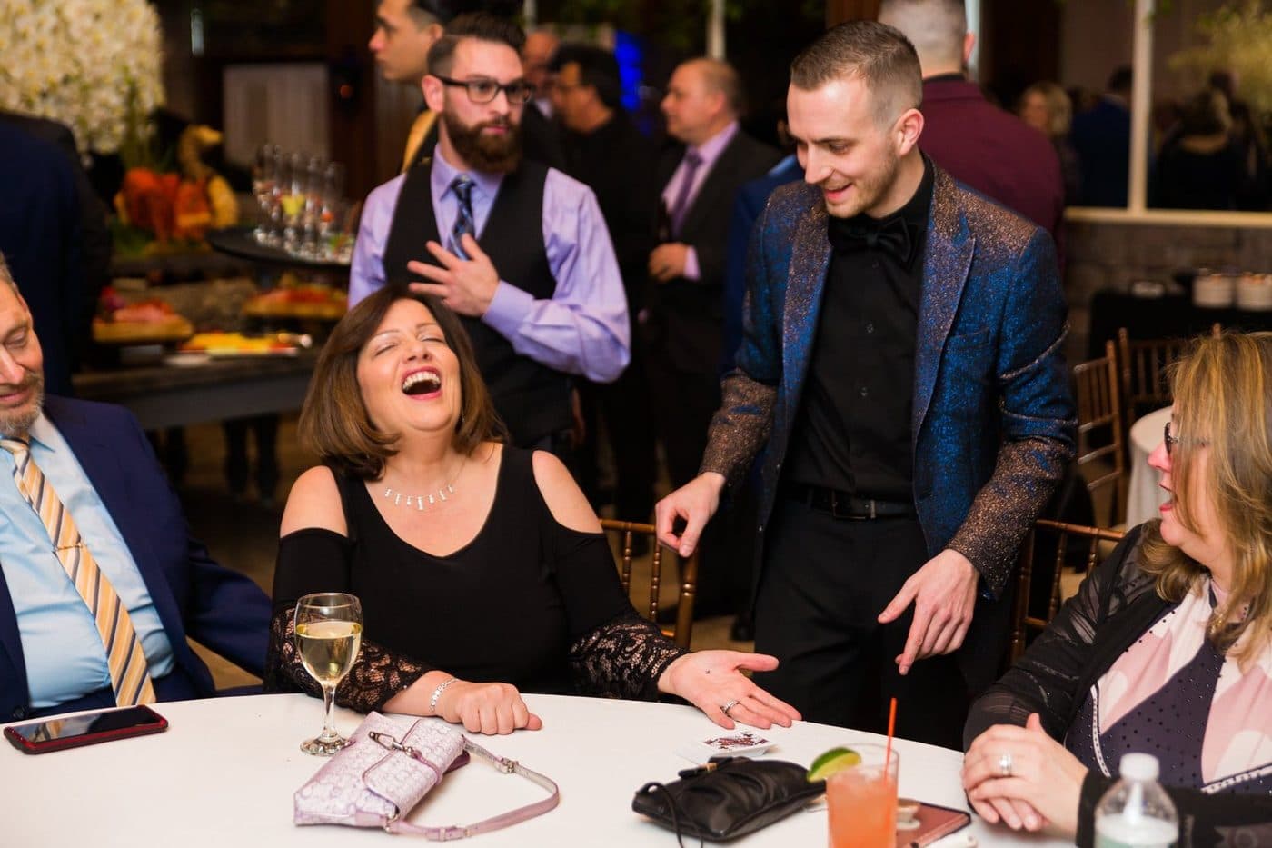 Guests at a banquet table laughing in amazement during a close-up magic performance.
