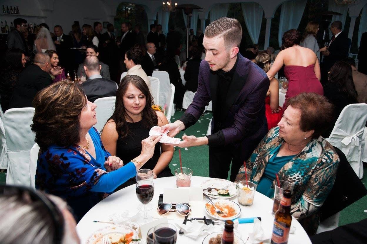 People laughing and enjoying a social gathering around a table with drinks and playing cards.