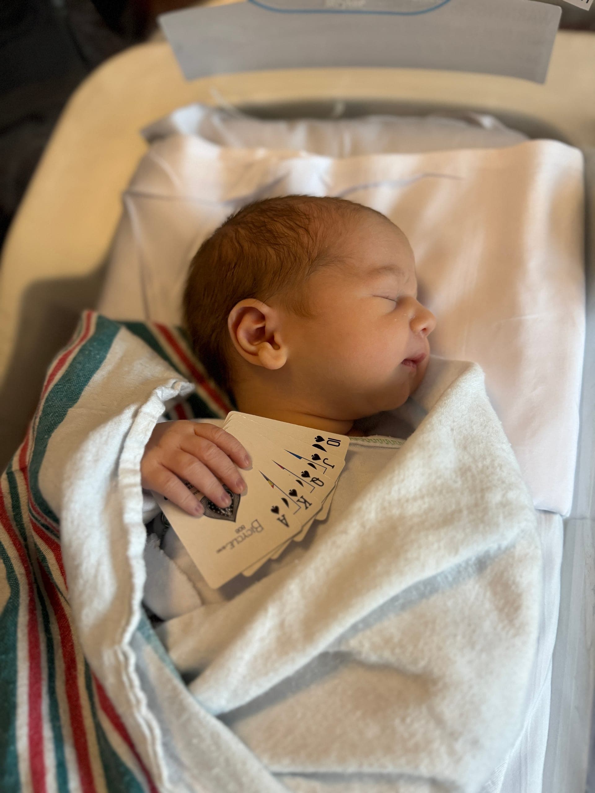 Newborn Brayden swaddled and holding a fan of playing cards