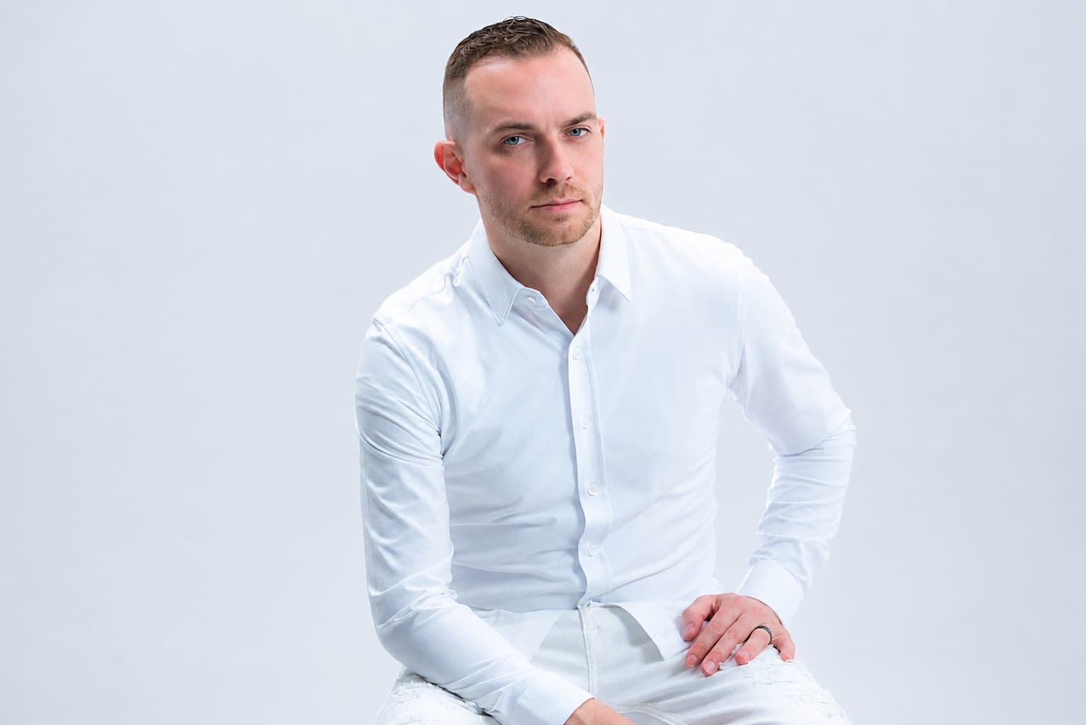 Chris Dare seated in a white shirt against a bright studio backdrop