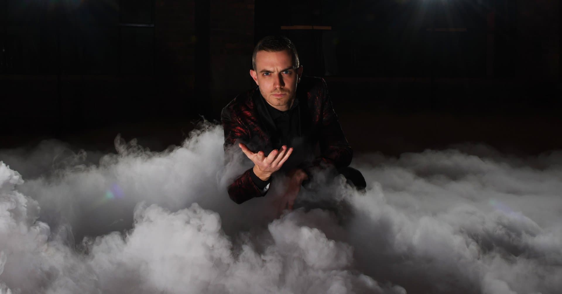 Chris Dare crouching in a red-and-black jacket amid rolling stage smoke