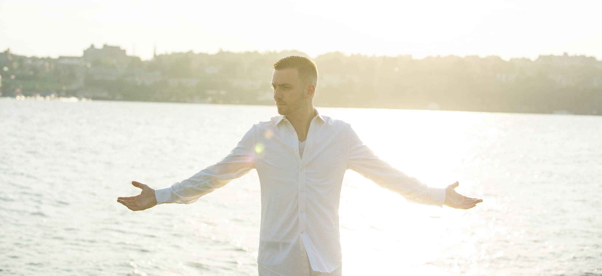 Chris Dare standing with arms outstretched by the water at sunset