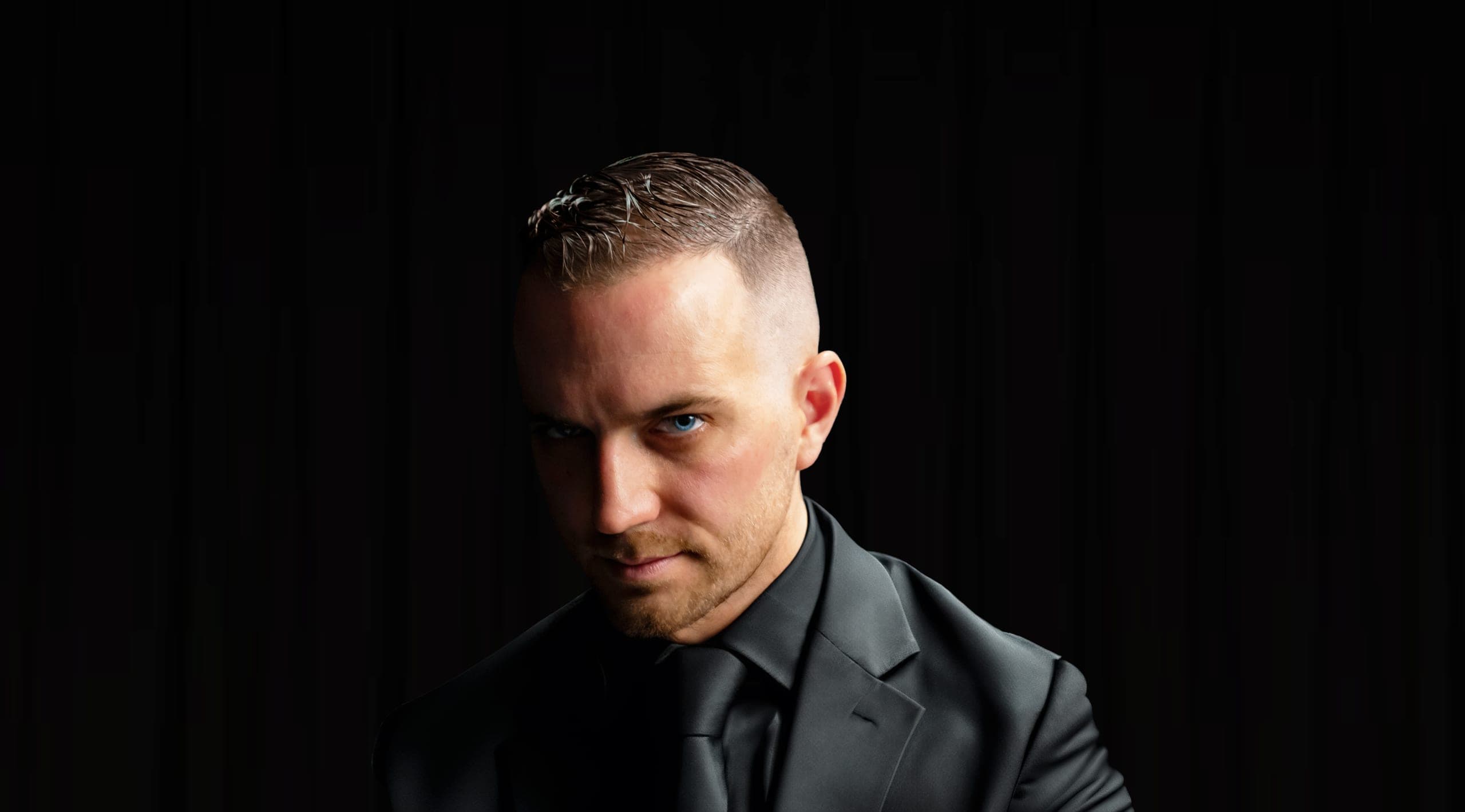 Chris Dare in a black suit against a dark background