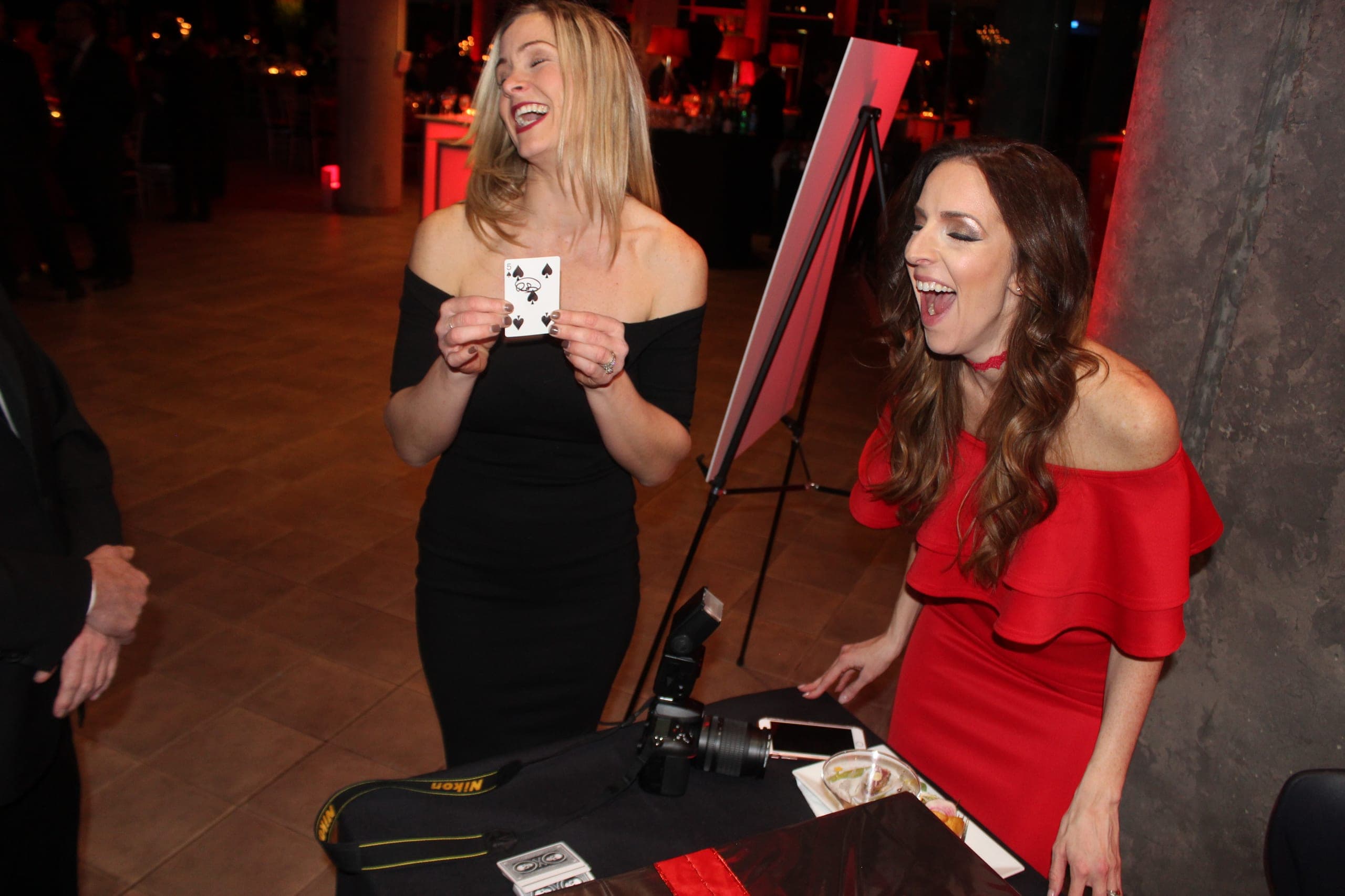 Two guests laughing as they hold a signed playing card from close-up magician Chris Dare at a New York gala