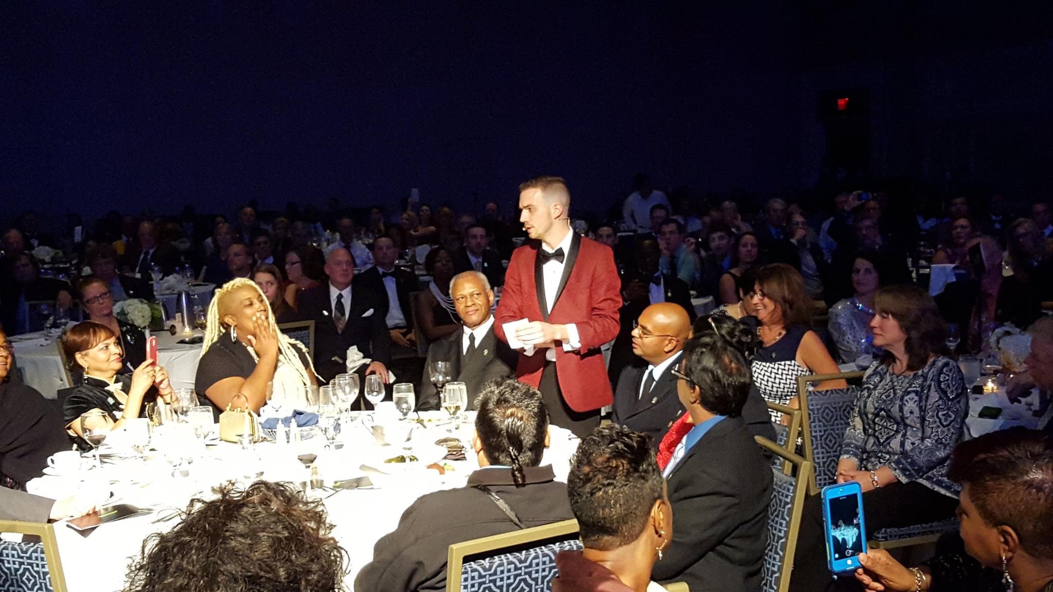 Chris Dare in a red dinner jacket performing his show among the tables of a packed corporate gala ballroom