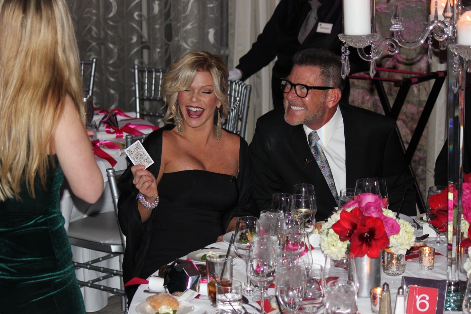 A guest holding a playing card and laughing at a gala dinner table